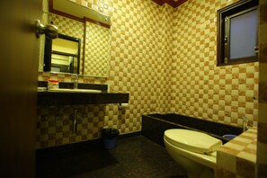 A bathroom with a checkered tile wall, a sink, a mirror, a toilet, and a bathtub. - Hotel Anandam (Gurugram)