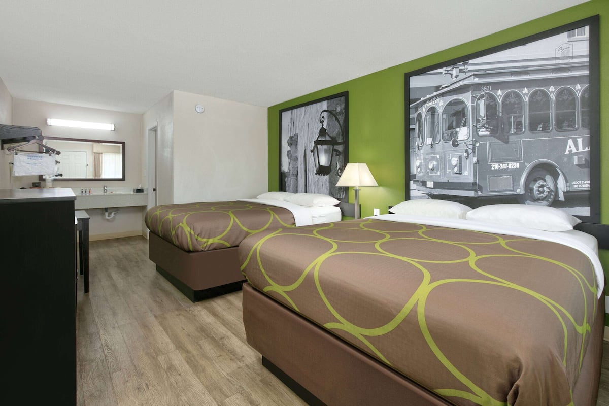 Ett hotellrum med två sängar, ett skrivbord, en spegel och en tv som är monterad på väggen.