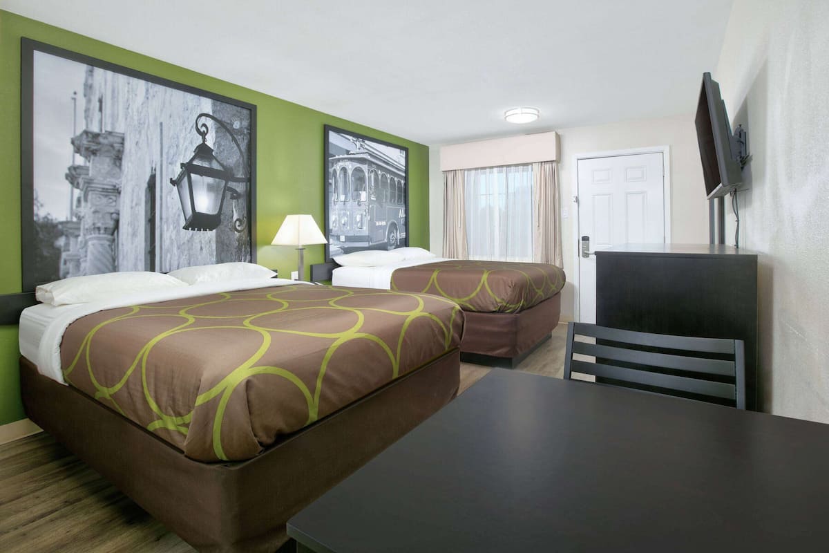 Ett hotellrum med två sängar, ett skrivbord, en stol, en TV och konstverk på väggarna.