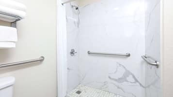 A bathroom with white marble walls, a shower with a handheld showerhead, and a grab bar for safety.