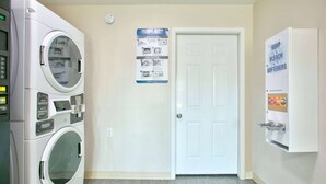 A laundry room with two front-loading washers and dryers, a door, and a wall-mounted soap dispenser. - Super 8 by Wyndham Palestine (Palestine)