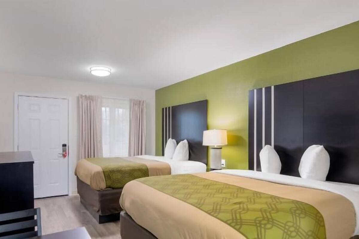 Ett hotellrum med två sängar, ett skrivbord, en TV och ett fönster med gardiner.