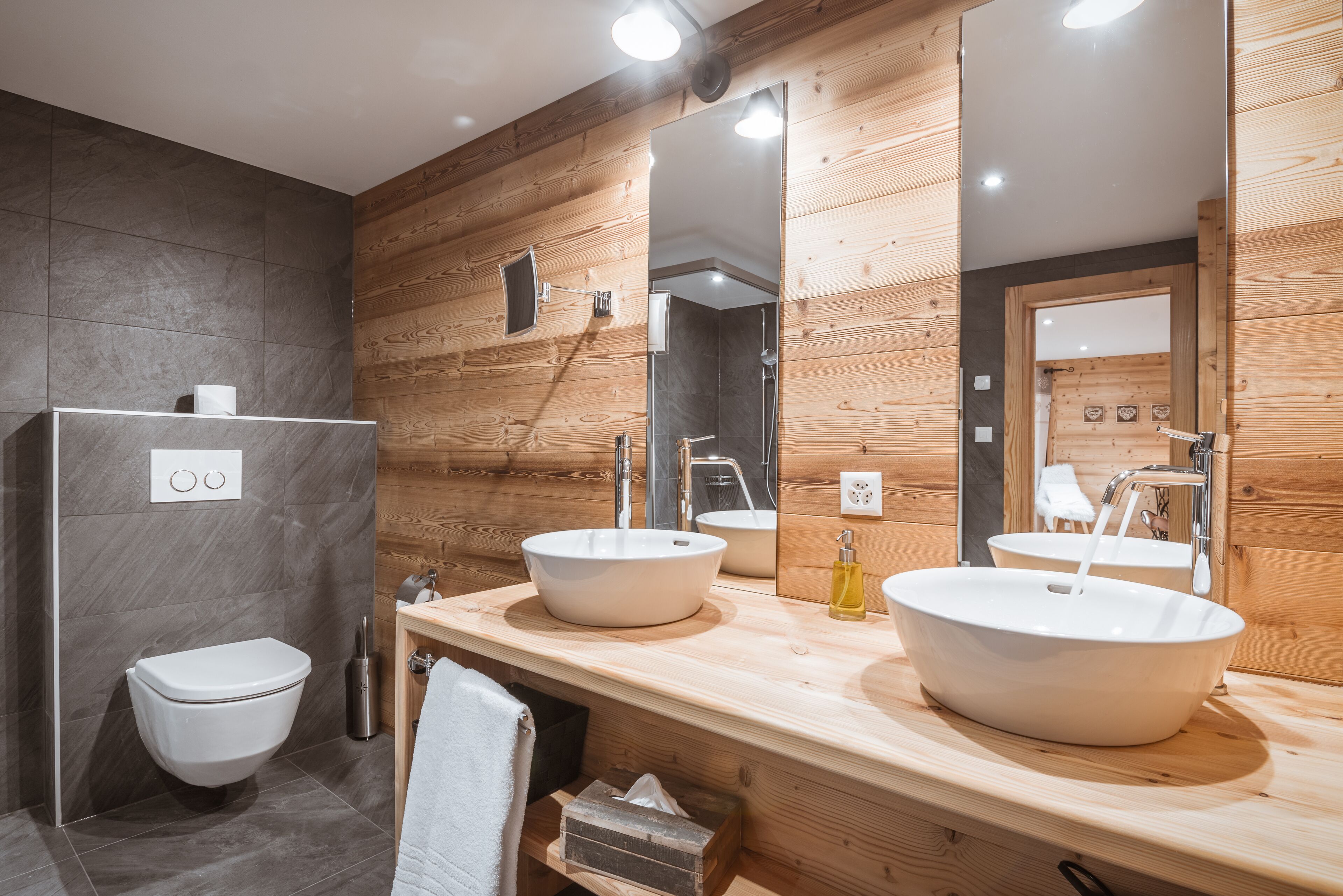 A modern bathroom with two sinks, a toilet, and wooden paneling.