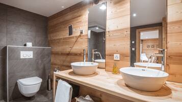 A modern bathroom with two sinks, a toilet, and wooden paneling.
