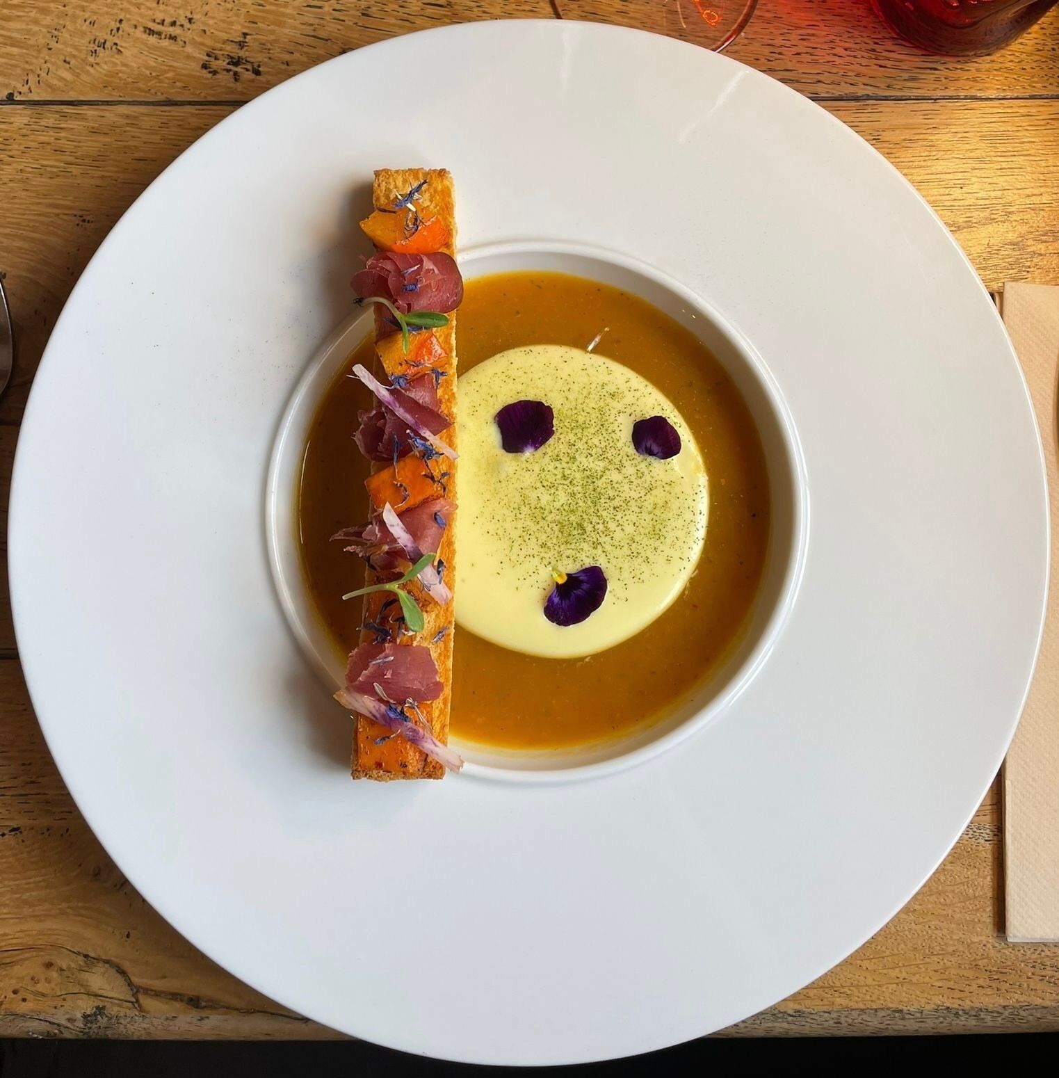 A white plate with a dessert featuring a yellow sphere and a decorative element on the side.