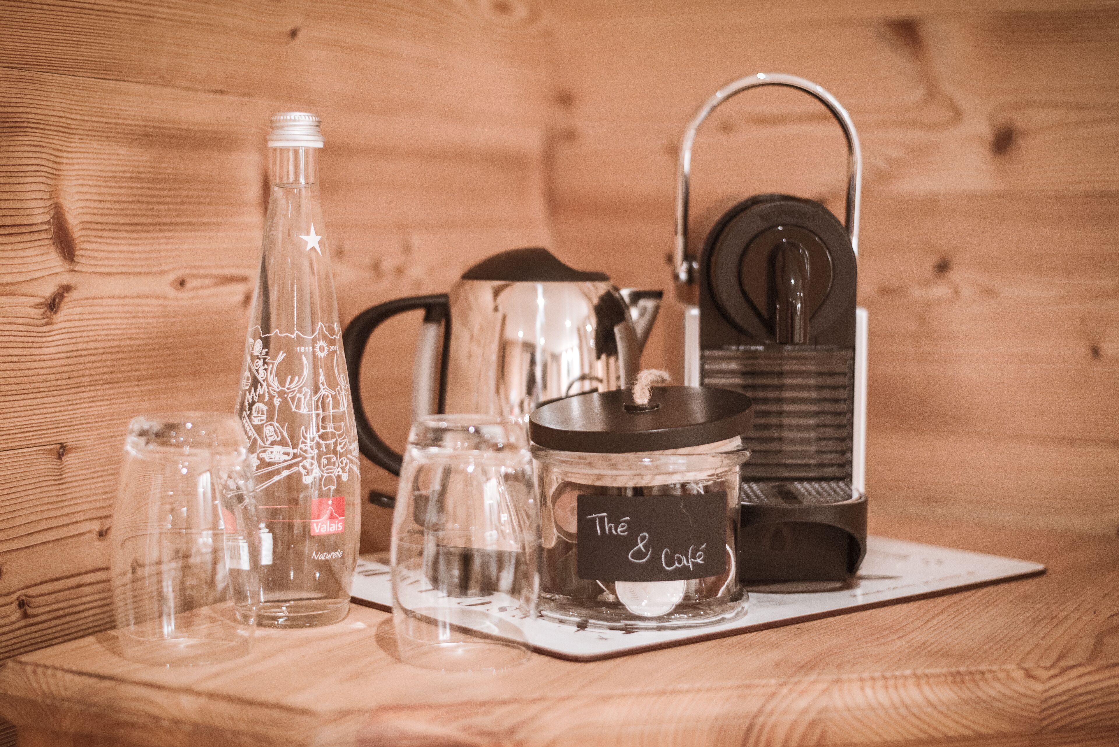 A wooden interior with a coffee maker, a kettle, and a glass bottle on a wooden table.