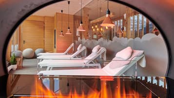 Relax in a serene spa room with a glass-enclosed view, three comfortable loungers, and a soothing fire feature.