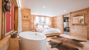A wooden cabin bedroom with a large bed, a wooden bathtub, and a cowhide rug.