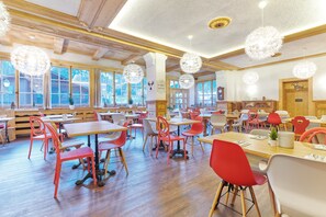 A spacious dining area with wooden tables and chairs, large windows, and decorative spherical light fixtures. - Lifestyle Rooms & Suites by Beau-Séjour (Champery)