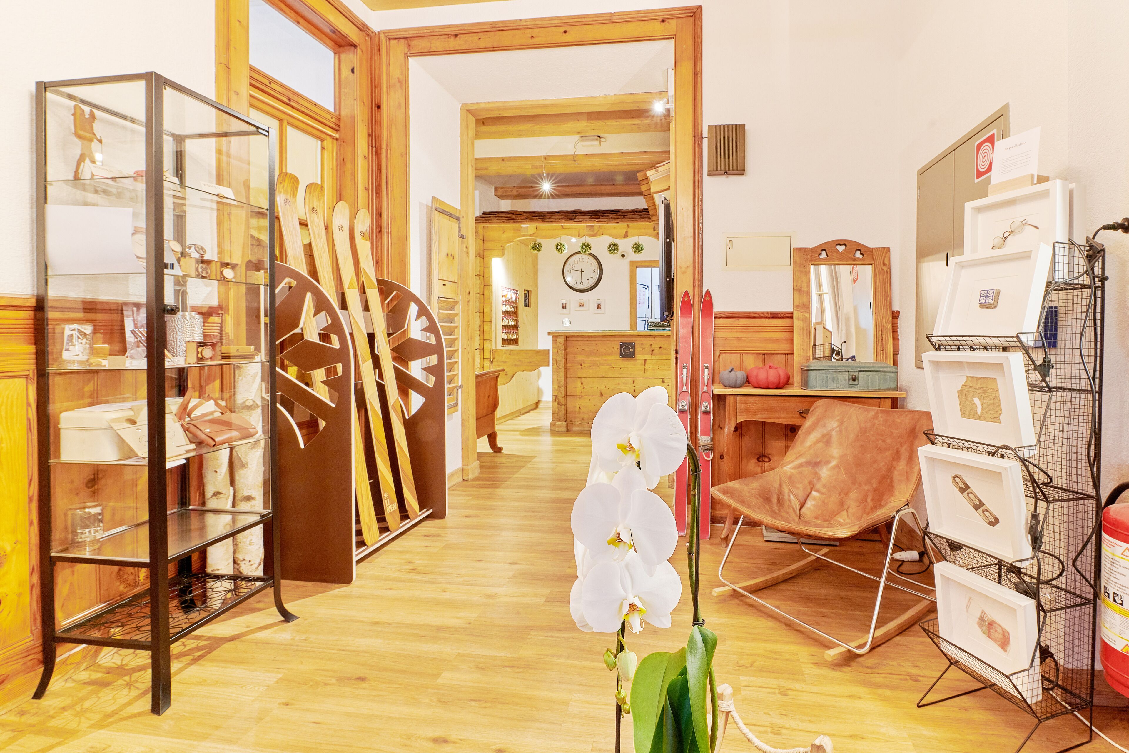 Una habitación con suelo de madera, una vitrina de cristal, un sillón de cuero marrón y una orquídea blanca.