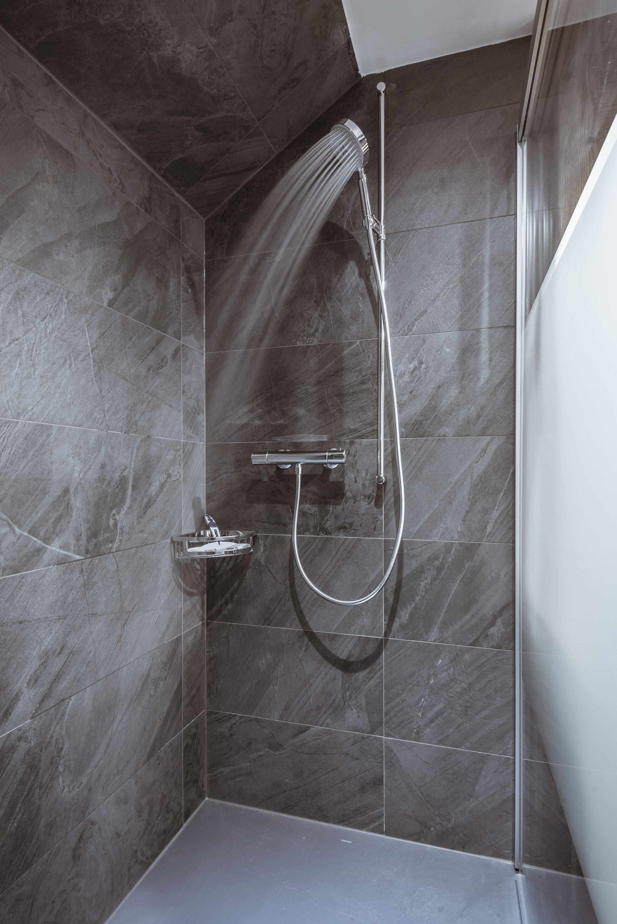 Una ducha moderna con cabezal de ducha de mano y mandos en la pared.