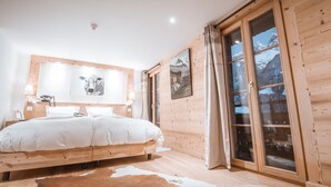A bedroom with a wooden bed, a cow print rug, and a large window with a mountain view.