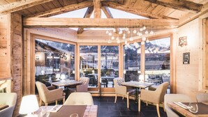 A wooden interior with large windows, tables, and chairs arranged for dining.