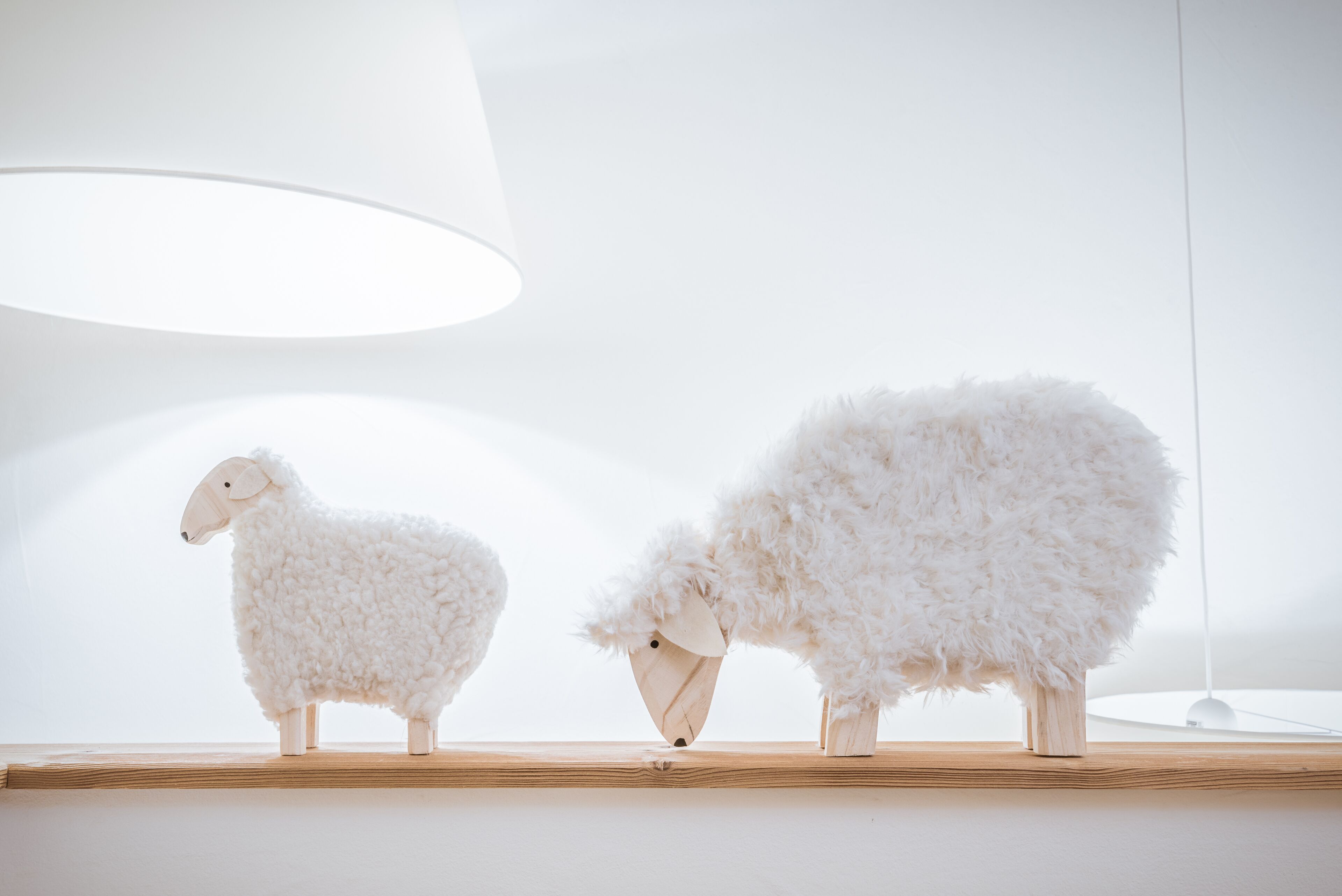 Deux petites figurines de moutons en bois, posées sur une étagère.