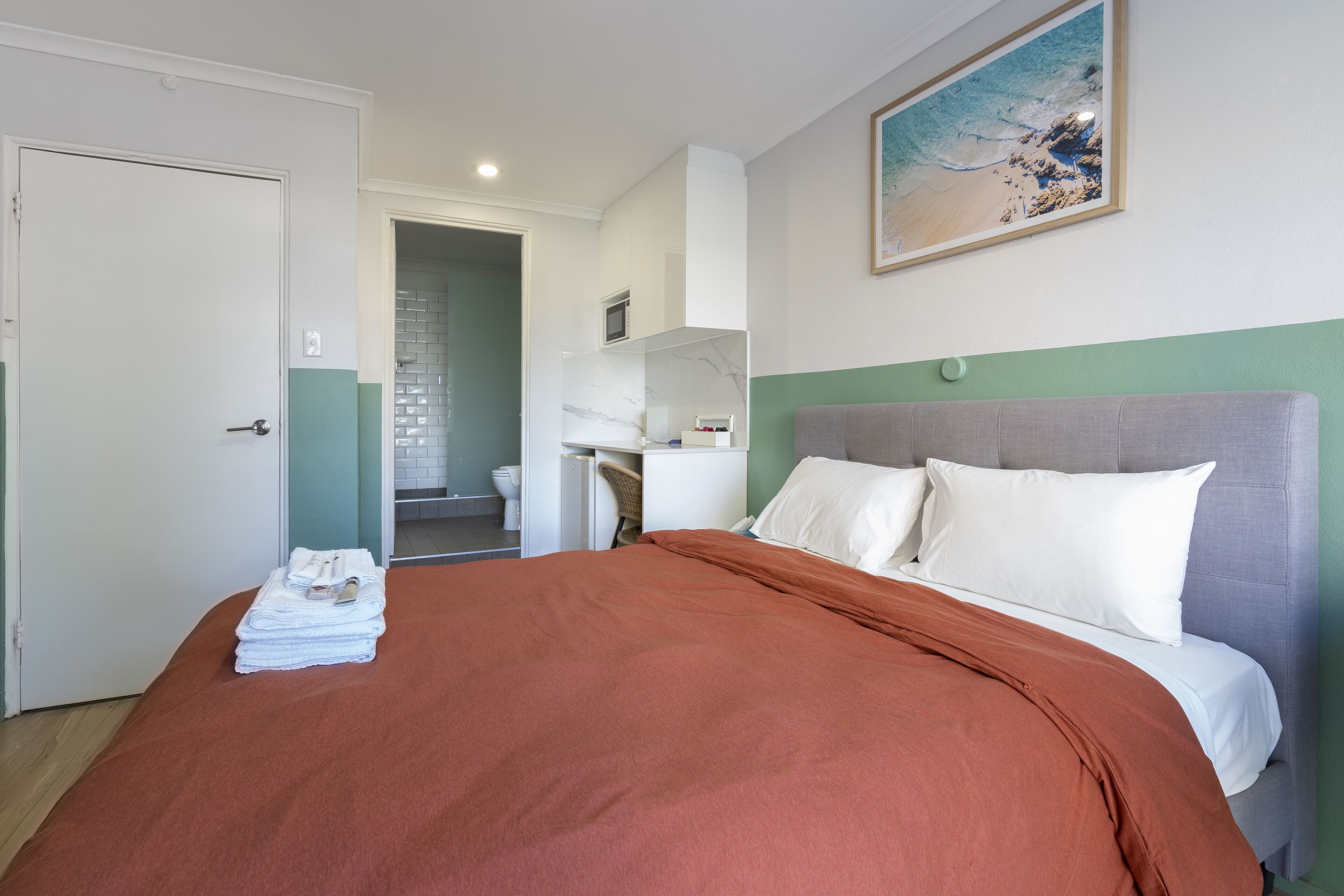 Una habitación de hotel con cama, escritorio y baño visible a través de una puerta abierta.