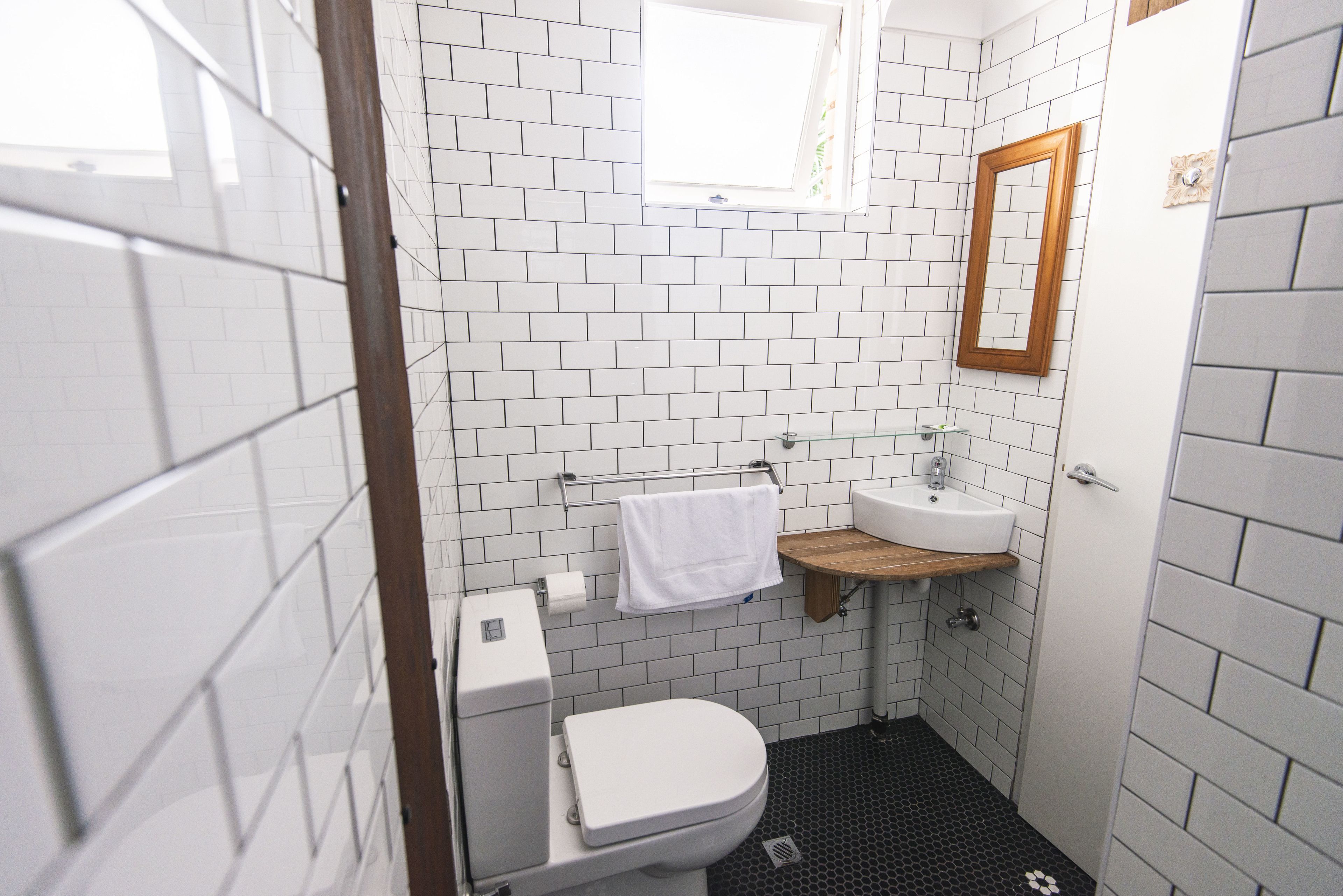 A small, modern bathroom with white subway tiles, a white toilet, a wooden vanity with a sink, and a mirror.