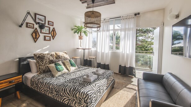 Een moderne slaapkamer met een bed met een zebraprint, een zwarte leren bank en een groot raam met gordijnen.