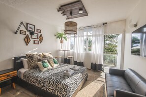 A modern bedroom with a zebra-patterned bed, a black leather sofa, and a large window with curtains. - Manly Waves Studios & Apartments (Manly)