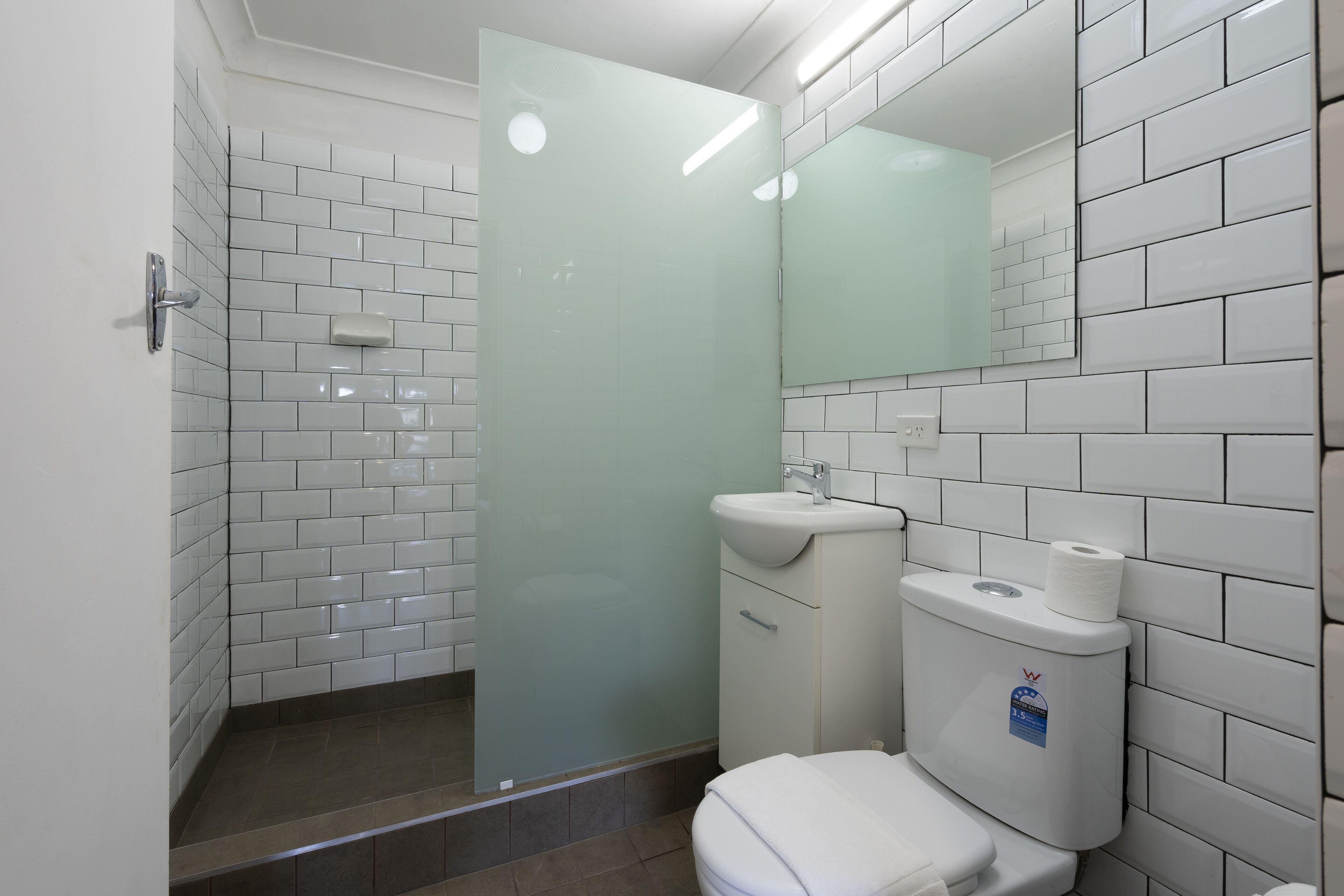 A bathroom with white tiled walls, a glass shower enclosure, a white sink, and a toilet.