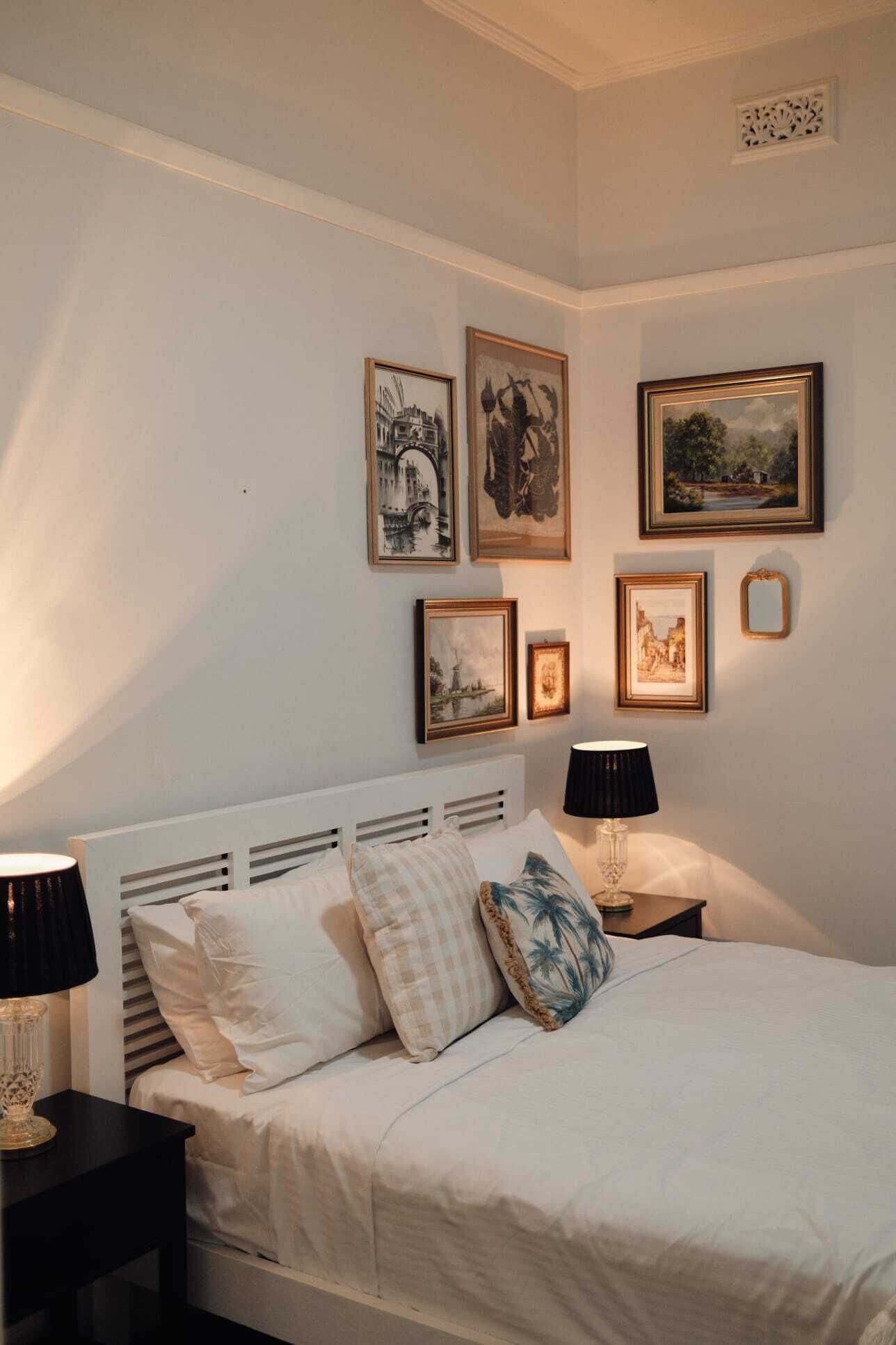 A bedroom with a white bed, multiple framed pictures on the wall, and two bedside lamps.