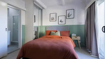 Habitación de hotel con cama, mesita de noche, ventana con cortinas y puerta que da a un baño.