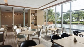 Un espace de restauration moderne, doté de tables et de chaises, de grandes fenêtres et offrant une vue sur la verdure environnante.