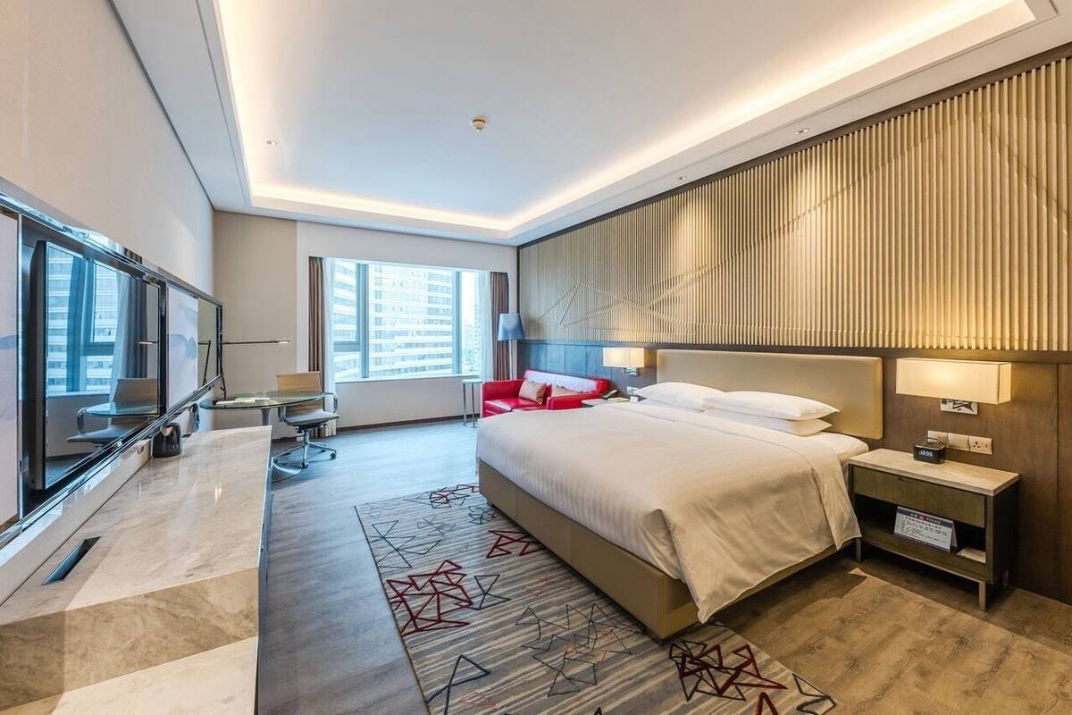 Une chambre d’hôtel moderne dotée d’un grand lit, d’un bureau, d’une télévision et offrant une vue sur la ville.