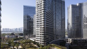 Un immeuble moderne de grande hauteur, doté d’une façade incurvée, entouré de verdure et d’autres bâtiments.
