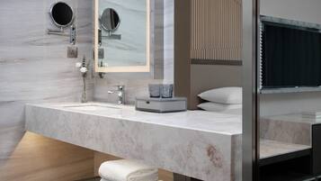A modern bathroom with a marble sink, two round mirrors, a towel rack, and a glass shelf.