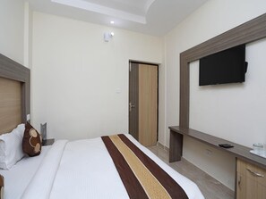 Une chambre d’hôtel avec un lit, un téléviseur fixé au mur, une porte en bois et une table de chevet.