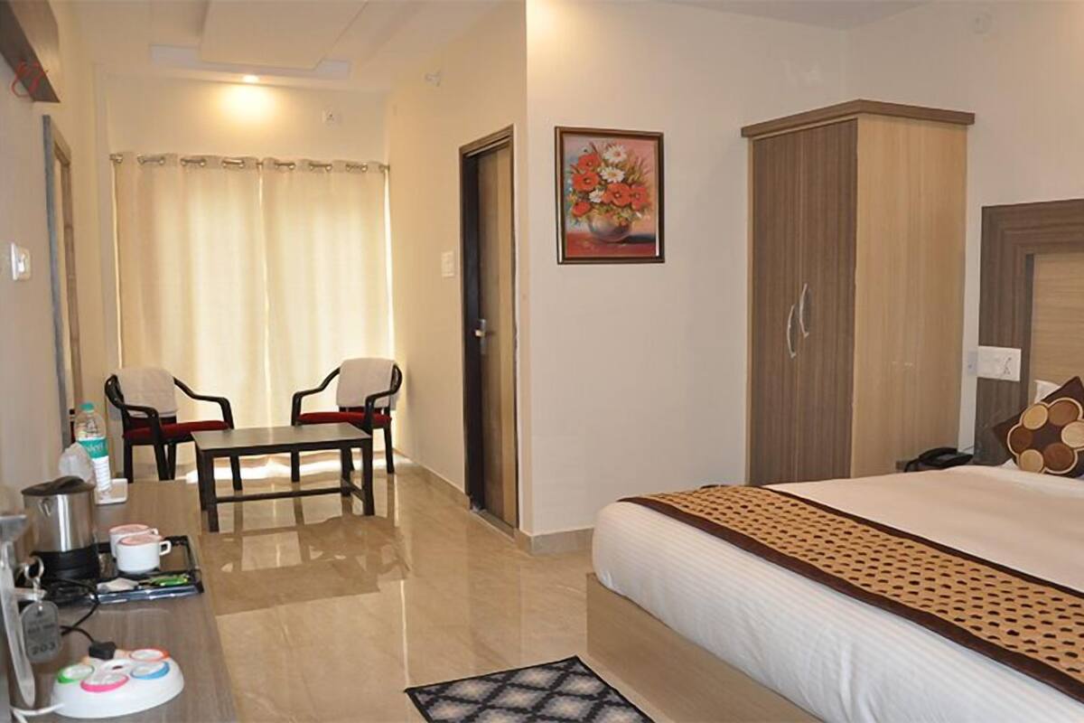 A hotel room with a bed, a desk with a chair, a wardrobe, and a painting on the wall.