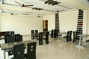 Un vaste espace dédié à la salle à manger, avec de nombreuses tables et chaises, des ventilateurs de plafond et un design moderne.