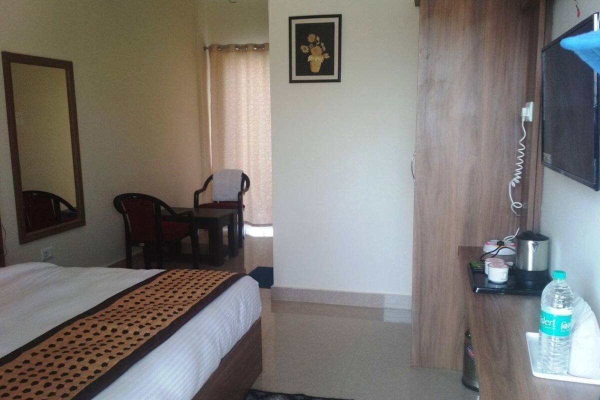 A hotel room with a bed, a desk, a chair, a television, a mirror, a picture on the wall, and a water bottle on the nightstand.