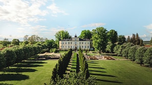 A large, symmetrical building with a central entrance, surrounded by well-manicured gardens and a clear sky. - Haga Slott (Enkoping)