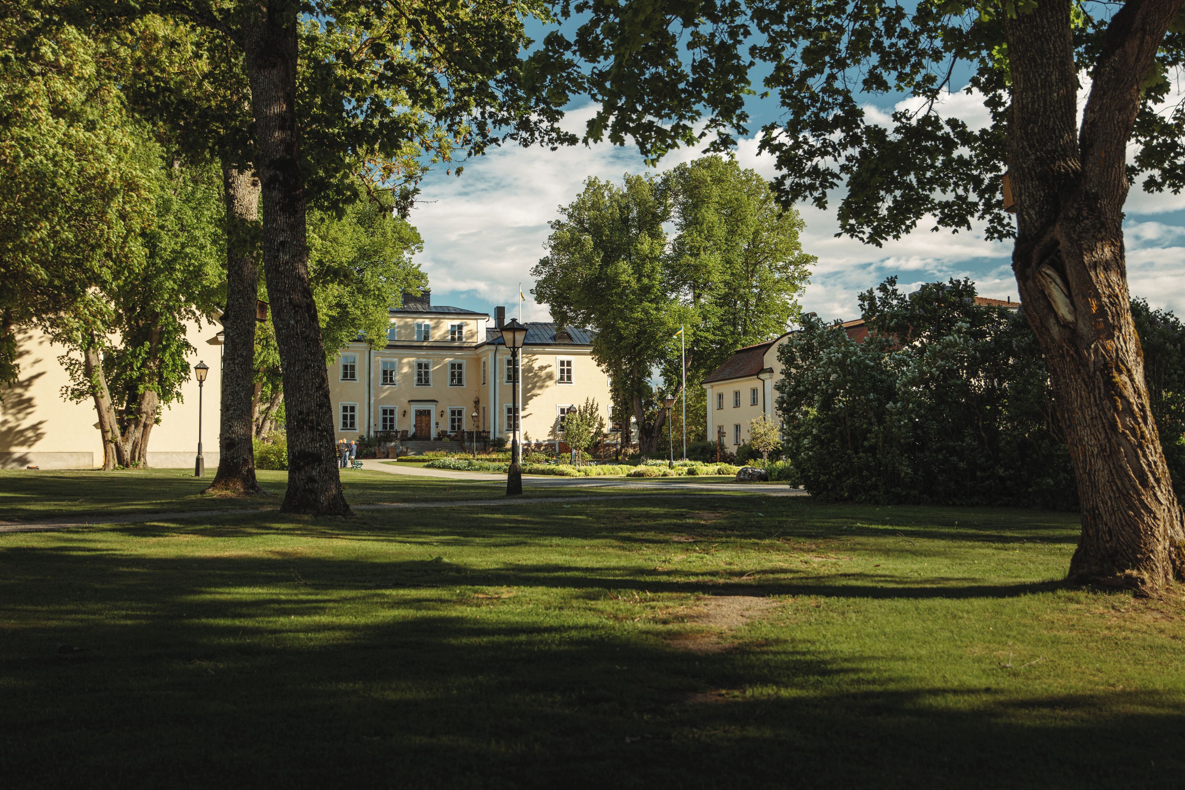 A park with mature trees, a well-maintained lawn, and a building with a classic architectural style in the background.