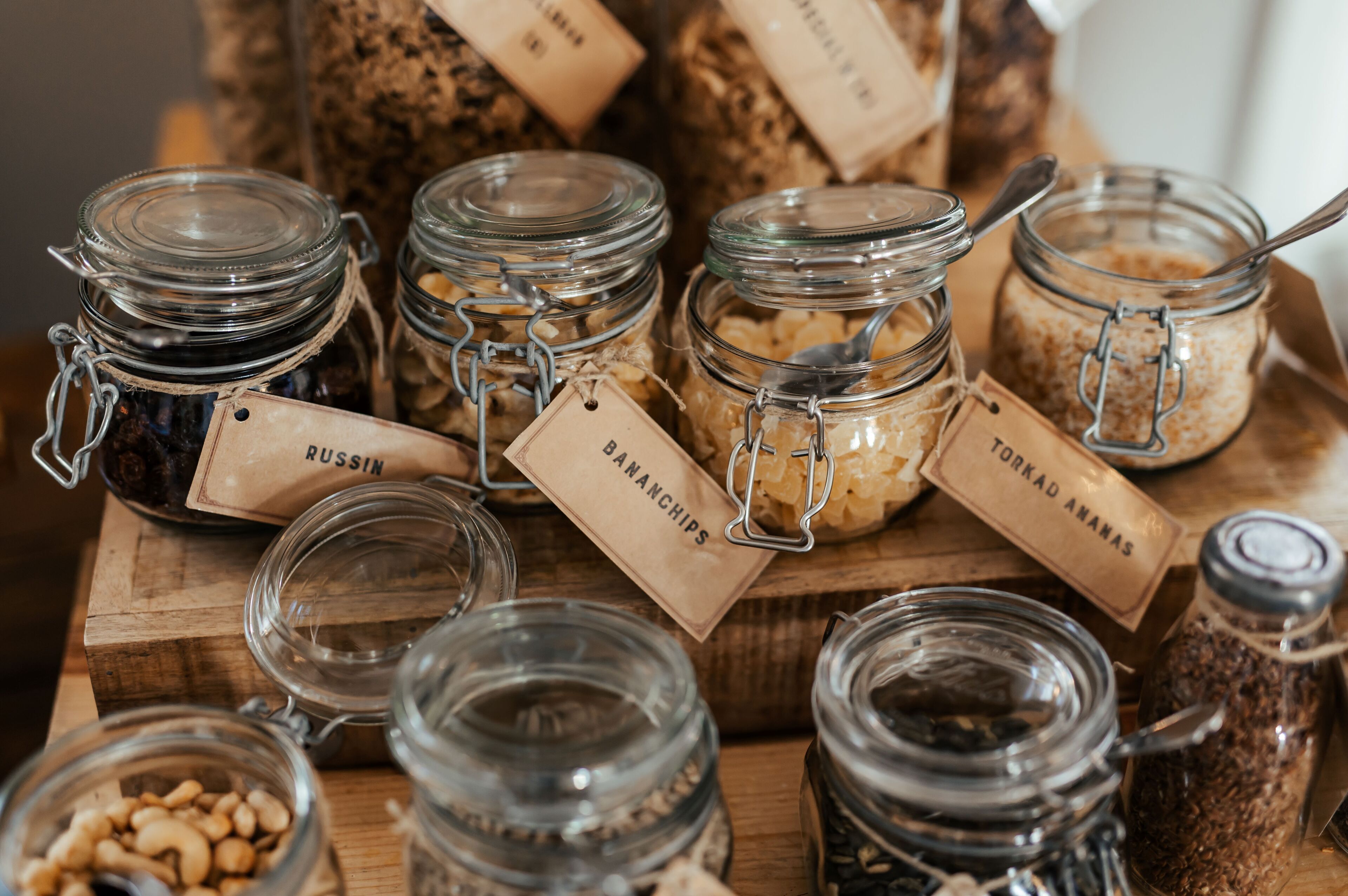 A variety of glass jars with labels on a wooden surface, likely containing different food items or condiments.