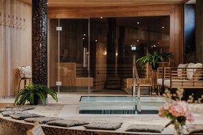 A modern spa area with a glass-enclosed hot tub, wooden seating, and a potted fern. - Haga Slott (Enkoping)
