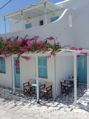 A white building with blue shutters and a covered outdoor seating area with tables and chairs. - Galanis Place (Antiparos)