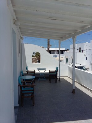 A covered outdoor seating area with a table and chairs, a small round table, and a view of the surrounding buildings. - Galanis Place (Antiparos)
