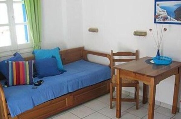 A small room with a wooden bed, a blue sofa, a wooden table, and a painting on the wall. - Galanis Place (Antiparos)