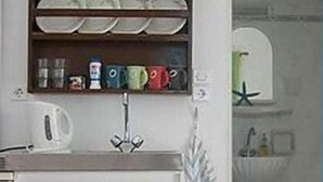 Una cocina con armarios blancos, un estante empotrado con vajilla, un hervidor y una decoración con una estrella de mar.