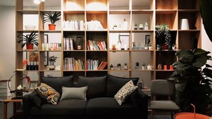 A modern living room with a black sofa, a wooden bookshelf filled with books and plants, and a small orange table. - xinyi (Huairou)