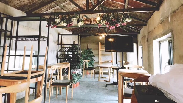 A rustic interior with exposed wooden beams, hanging floral arrangements, and a central seating area with tables and chairs. - xinyi (Huairou)