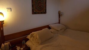 A hotel room with a bed, pillows, a nightstand with a lamp, a wall clock, and a decorative wall hanging. - Kichu Resort (Wangdue Phodrang)