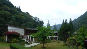 A courtyard with a stone pathway, a small building with a staircase, and a lush green garden. - Kichu Resort (Wangdue Phodrang)