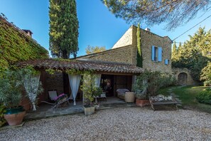 Charming countryside home with a rustic stone exterior, surrounded by lush greenery and a gravel driveway.