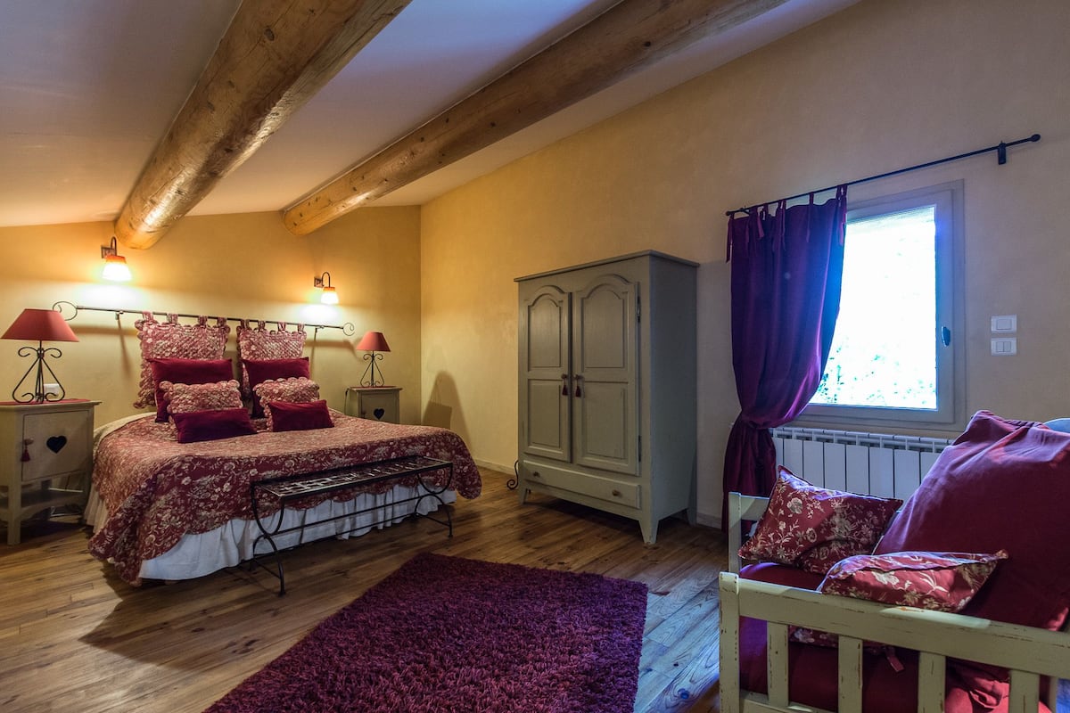 A bedroom with a bed, a wardrobe, a nightstand, and a window with curtains.
