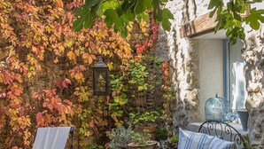 Une terrasse avec deux chaises en métal, une table et un mur de pierre recouvert de feuilles d’automne.