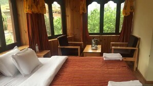 A hotel room with a large bed, two chairs, a small table with a kettle, and curtains. - Ngayabling Resort (Paro)