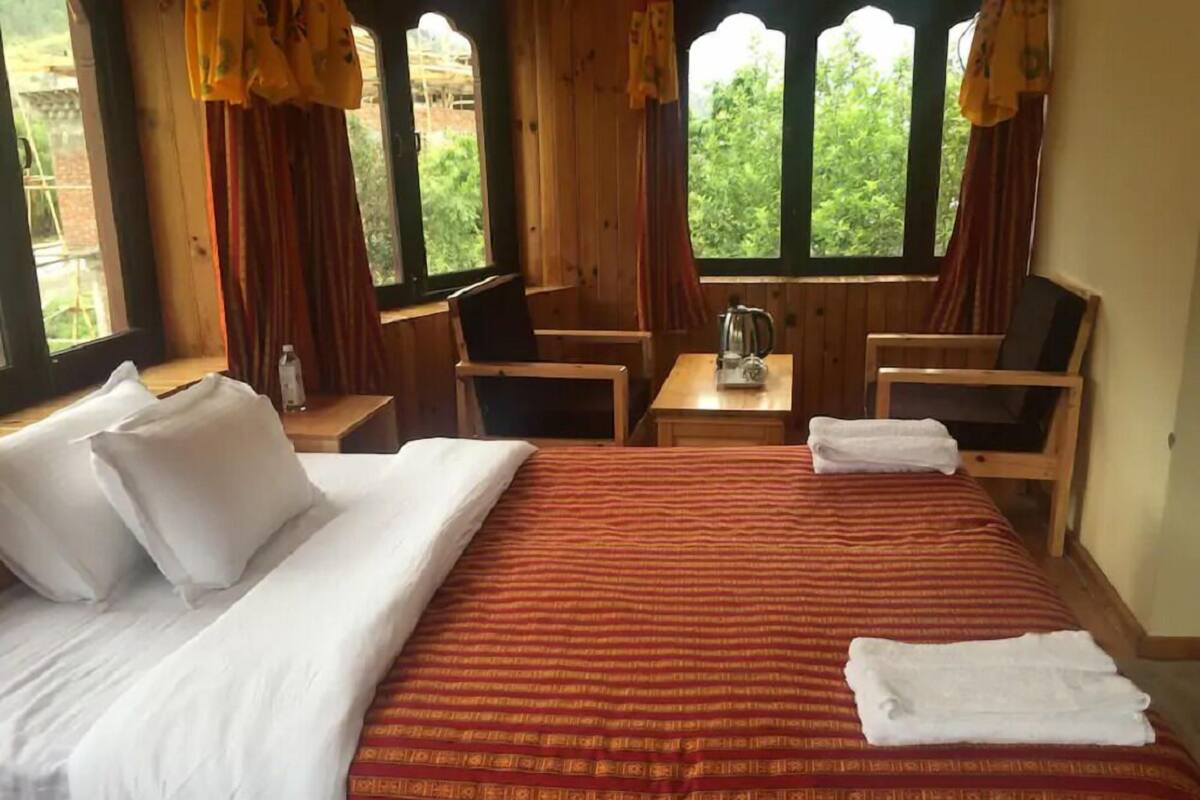 A hotel room with a large bed, two chairs, a small table with a kettle, and curtains.